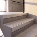 Satin Silver rake back DDA aluminium stair nosing 70 x 56mm with Everest light grey Exterior Grip insert, fitted on raked concrete stairs in a commercial stairwell