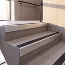 Satin Silver rake back DDA aluminium stair nosing 70 x 56mm with Obsidian black High Grip insert, fitted on raked concrete stairs in a commercial stairwell