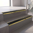 Square edge with ramped back aluminium stair nosing, 70mm tread, coal (black) exterior grip insert, mirrorflect gold finish