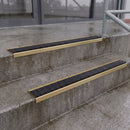 Square edge with ramped back aluminium stair nosing with black gritted exterior grip insert in satin gold finish fitted on covered external concrete steps