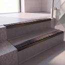 Square edge with ramped back aluminium stair nosing with a dark charcoal Mor Grip insert in dark bronze finish fitted on a retail unit stair finished in grey vinyl