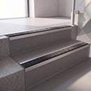 Square edge with ramped back aluminium stair nosing with a dark charcoal Mor Grip insert in mill finish finish fitted on a retail unit stair finished in grey vinyl
