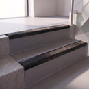 Square edge with ramped back aluminium stair nosing with a dark charcoal Mor Grip insert in satin black finish fitted on a retail unit stair finished in grey vinyl
