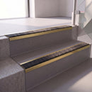 Square edge with ramped back aluminium stair nosing with a dark charcoal Mor Grip insert in satin gold finish fitted on a retail unit stair finished in grey vinyl