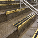 Square edge with ramped back aluminium stair nosing with black gritted exterior grip insert in mirrorflect gold finish fitted on covered external concrete steps