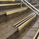 Square edge with ramped back aluminium stair nosing with black gritted exterior grip insert in satin gold finish fitted on covered external concrete steps