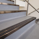Square edge with ramped back aluminium stair nosing with twin dark charcoal Mor Grip inserts in dark bronze finish fitted on a leisure centre stair finished in grey safety vinyl