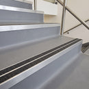 Square edge with ramped back aluminium stair nosing with twin dark charcoal Mor Grip inserts in mill finish finish fitted on a leisure centre stair finished in grey safety vinyl