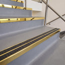 Square edge with ramped back aluminium stair nosing with twin dark charcoal Mor Grip inserts in mirrorflect gold finish fitted on a leisure centre stair finished in grey safety vinyl