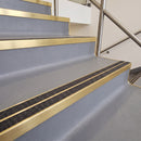 Square edge with ramped back aluminium stair nosing with twin dark charcoal Mor Grip inserts in satin gold finish fitted on a leisure centre stair finished in grey safety vinyl