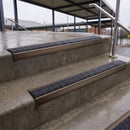 Square edge with ramped back aluminium stair nosing with black gritted exterior grip insert in dark bronze finish fitted on covered external concrete steps