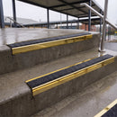 Square edge with ramped back aluminium stair nosing with black gritted exterior grip insert in mirrorflect gold finish fitted on covered external concrete steps