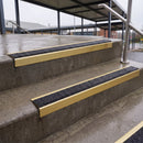 Square edge with ramped back aluminium stair nosing with black gritted exterior grip insert in satin gold finish fitted on covered external concrete steps