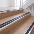 Ramp back twin channel aluminium stair nosing 93 x 38mm in Bright Polished with two Obsidian textured High Grip inserts, fitted on an indoor oak-effect vinyl staircase