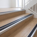 Ramp back twin channel aluminium stair nosing 93 x 38mm in Mill Finish with two Obsidian textured High Grip inserts, fitted on an indoor oak-effect vinyl staircase