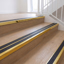 Ramp back twin channel aluminium stair nosing 93 x 38mm in Mirrorflect Gold with two Obsidian textured High Grip inserts, fitted on an indoor oak-effect vinyl staircase