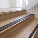 Ramp back twin channel aluminium stair nosing 93 x 38mm in Satin Bronze with two Obsidian textured High Grip inserts, fitted on an indoor oak-effect vinyl staircase