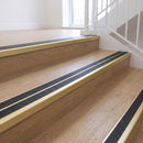 Ramp back twin channel aluminium stair nosing 93 x 38mm in Satin Gold with two Obsidian textured High Grip inserts, fitted on an indoor oak-effect vinyl staircase