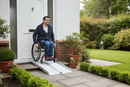 Portable folding aluminium wheelchair ramp deployed over a front doorstep with a wheelchair user approaching the door