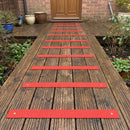 Red 90mm fine grit GRP anti-slip decking strips screwed across a garden decking walkway