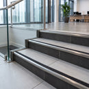 Retro-fit stainless steel stair nosing with GS Black RAL 9011 R11 grit tread capping the step edges of a tiled office lobby stair