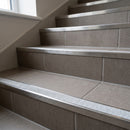 Retro-fit stainless steel stair nosing with T Transparent R11 clear grit tread on warm grey tiled apartment stairs