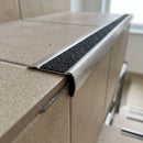 Close-up of the retro-fit stair nosing bonded over an existing tiled step, showing the rounded stainless nose, mineral grit tread and feathered rear edge