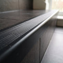 Close-up of the ribbed anti-slip tread and downturn of a black flexible PVC stair nosing fitted to a tiled step
