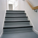 Black retrofit PVC stair nosings bonded to the edge of each step on a grey vinyl staircase in a communal building
