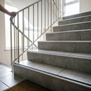 Retro-fit stainless steel stair nosing with black anti-slip tread bonded to existing grey tiled steps in an apartment block stairwell