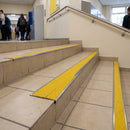 Retro-fit stainless steel stair nosing with yellow anti-slip tread on existing tiled steps in a school corridor