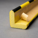Cut end of the L-shaped foam profile showing both legs and the adhesive strip with the release liner peeled back