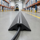 Single channel rubber cable ramp unrolled along a warehouse aisle with a black power cable running through its channel, pallet racking and a forklift in the background