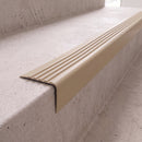 Beige 40x40mm flexible PVC angle stair nosing fitted directly to the bare concrete step edge of a daylit stairwell, showing the rounded nose and fluted anti-slip tread