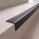 Black 40x40mm flexible PVC angle stair nosing fitted directly to the bare concrete step edge of a daylit stairwell, showing the rounded nose and fluted anti-slip tread