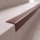 Brown 40x40mm flexible PVC angle stair nosing fitted directly to the bare concrete step edge of a daylit stairwell, showing the rounded nose and fluted anti-slip tread