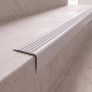 Pale grey 40x40mm flexible PVC angle stair nosing fitted directly to the bare concrete step edge of a daylit stairwell, showing the rounded nose and fluted anti-slip tread