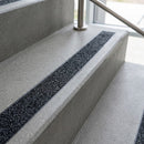 Close-up of a concrete step edge with a black grit anti-slip strip recessed into the tread