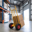 Yellow 200kg sack truck loaded with two cardboard boxes in a warehouse beside blue and orange pallet racking and an open loading bay door