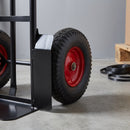 Close-up of the sack truck's 300mm pneumatic tyre on a red steel rim, the black steel wheel guard and the welded black steel toe plate resting on a concrete warehouse floor