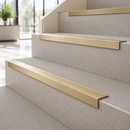 Satin brass ridged stair nosings fitted to pale stone steps in a daylit stairwell