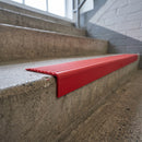 Close-up of red PVC stair nosing wrapping the edge of a concrete step, showing the ribbed anti-slip tread face