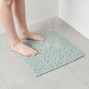 Sage green PVC pebble-textured non-slip shower mat with suction cups on a walk-in shower floor, with wet bare feet stepping onto it under running water