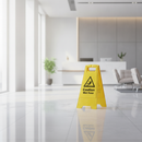 Yellow A-frame caution wet floor warning sign standing on a polished floor in a bright office corridor
