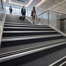 Silver aluminium stair nosing with black rubber inserts fitted full width on dark carpeted stairs in an airport terminal
