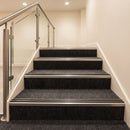 Silver aluminium stair nosing with twin black rubber inserts fitted full width on dark contract carpet stairs in a commercial interior