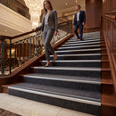 Silver aluminium stair nosing with black rubber inserts on a dark carpeted hotel staircase