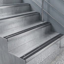 Silver anodised nosings screw-fixed flush to pale stone stair treads, viewed down a modern staircase