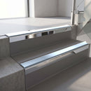 Square-edge aluminium stair nosing with a deep 56mm riser face in Bright Polished, fitted along two vinyl-covered concrete steps in an office stairwell, with an Aura anti-slip PVC insert running the full width of each step