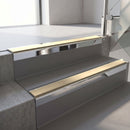 Square-edge aluminium stair nosing with a deep 56mm riser face in Bright Polished, fitted along two vinyl-covered concrete steps in an office stairwell, with a Beige anti-slip PVC insert running the full width of each step